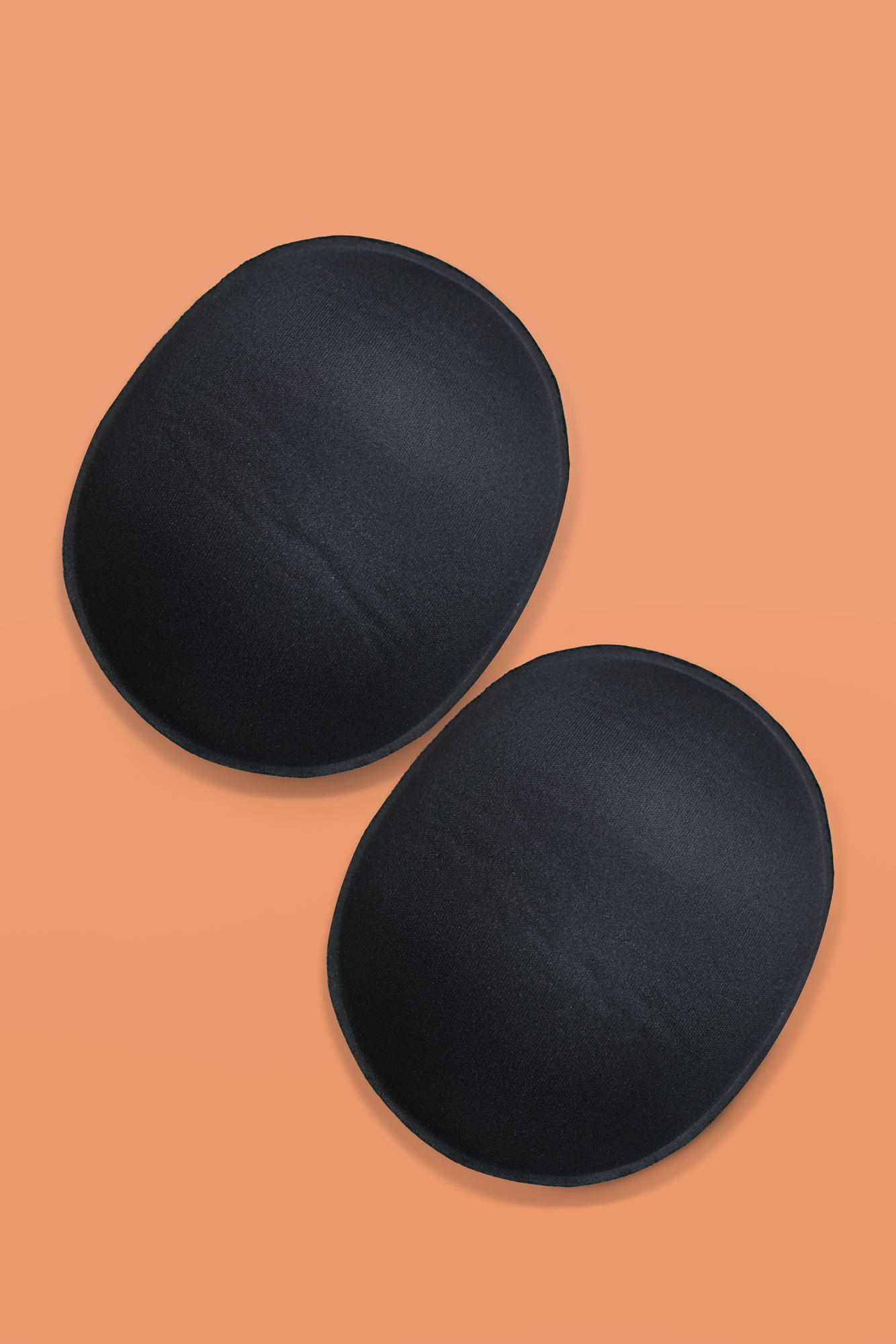 A pair of black cloth-covered oval-shaped foam pads for butt or hips on peach background.
