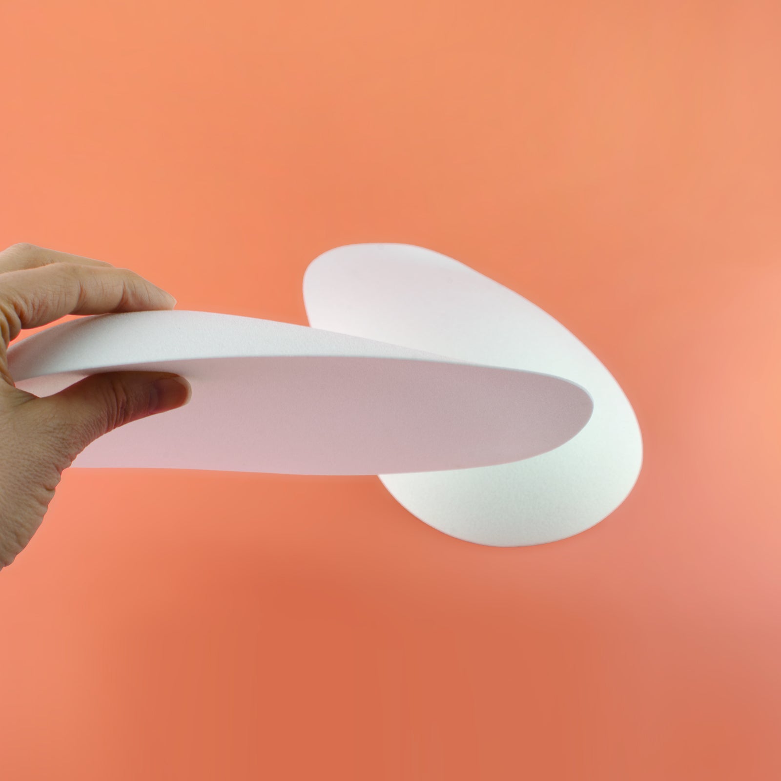 Hand holding a white butt foam pad against an peach background